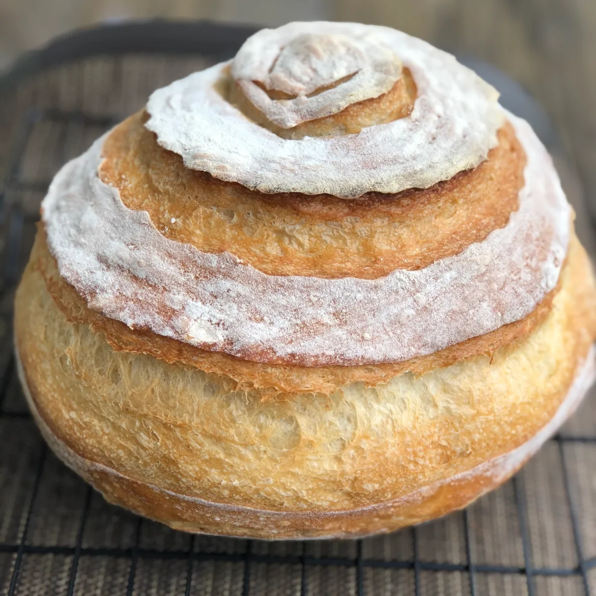 Close-up of a crusty white bread boule with a golden, spiraled crust, resting on a cooling rack.