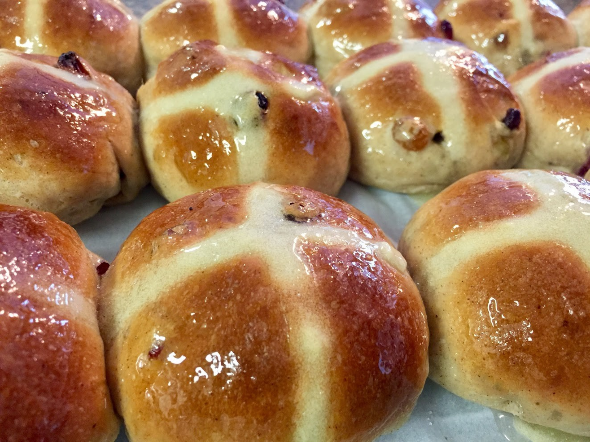 Freshly baked hot cross buns with a glossy glaze, golden-brown tops, and traditional cross markings, studded with raisins.